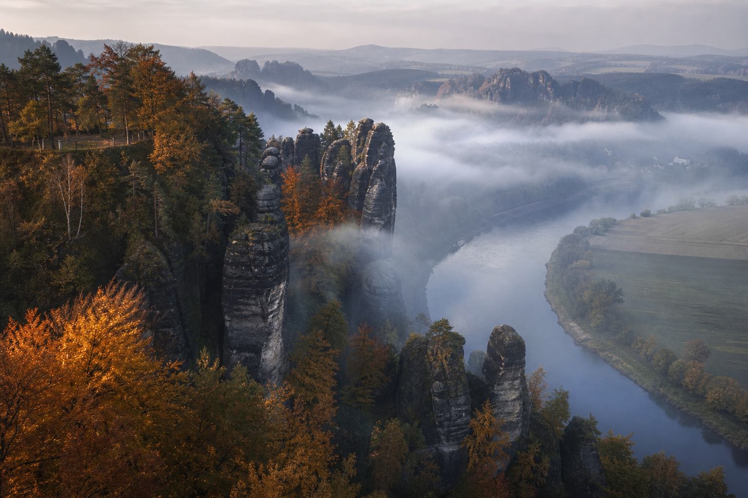 Herbstnebel und kupferfarbener Wald zwischen Sandsteintürmen über der Elbe